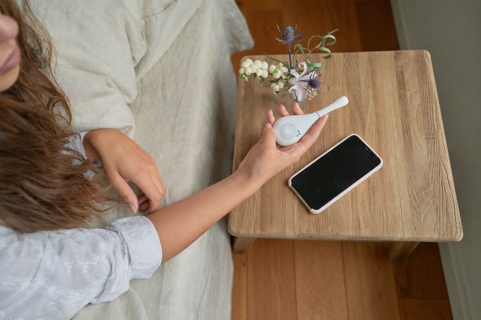 Daysy fertility tracker on wooden bedside table with smartphone and flowers