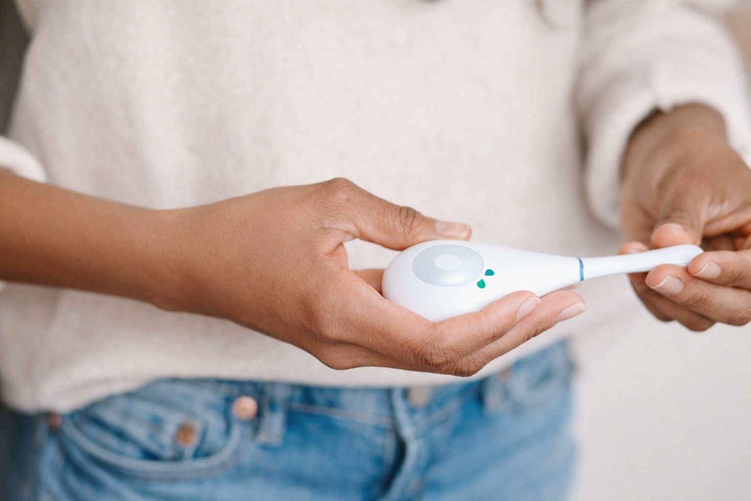 Close-up of Daysy fertility tracker cradled in both hands showing sensor base and green LED indicator