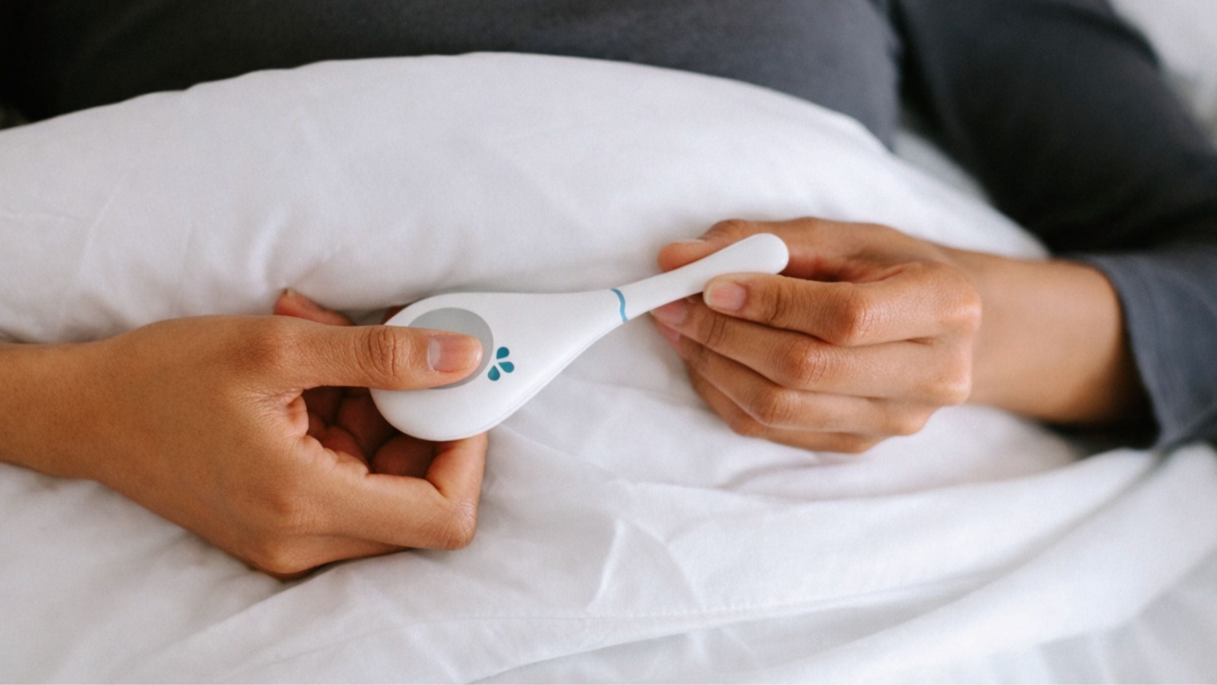 Woman holding Daysy fertility tracker in bed during morning BBT measurement