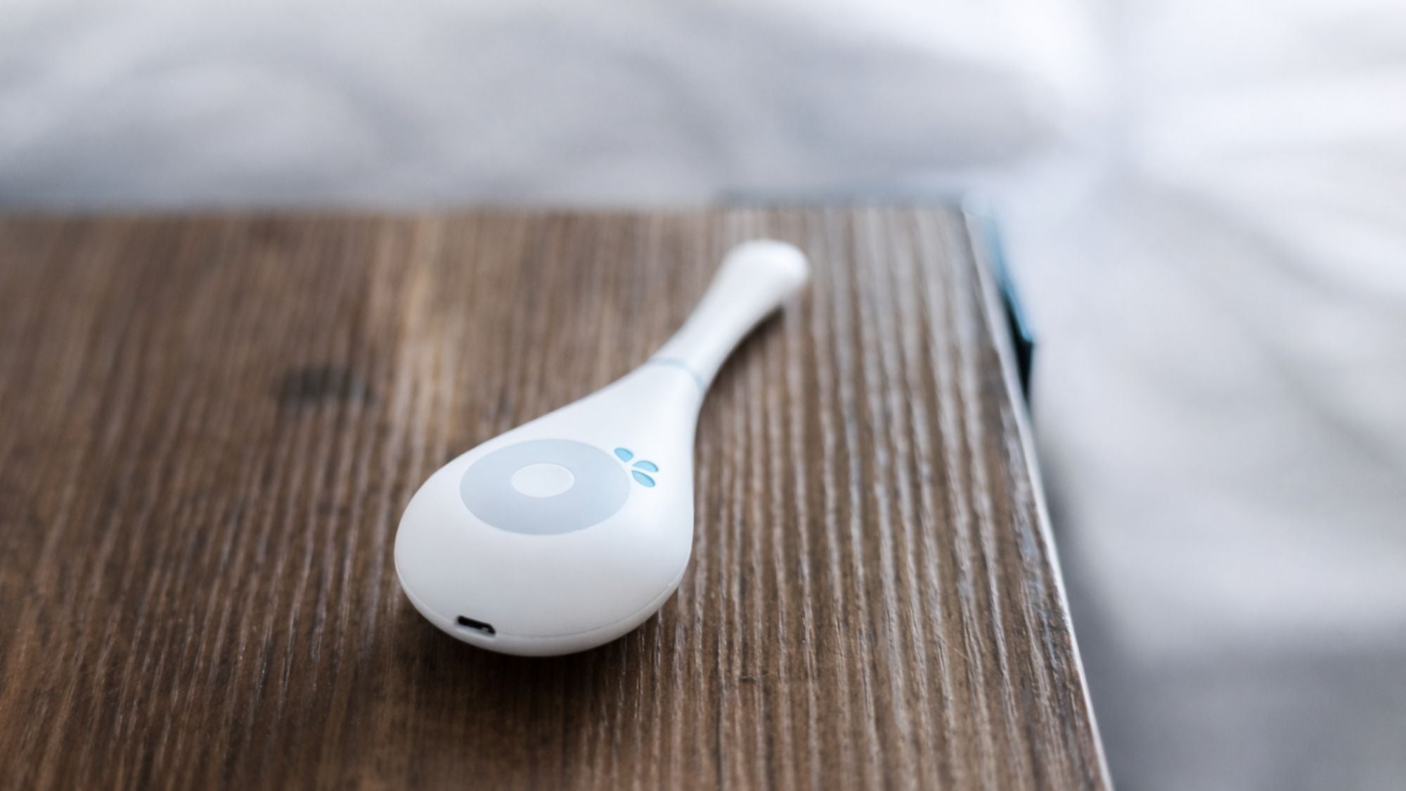Daysy fertility tracker resting on wooden bedside table showing USB charging port and teal LED indicator