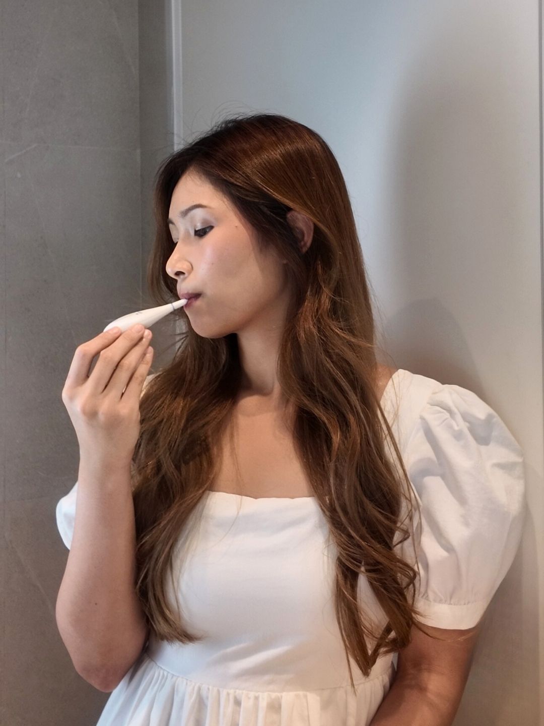 Side view of Asian woman placing Daysy fertility tracker in her mouth, showing how the product is used as part of fertility tracking