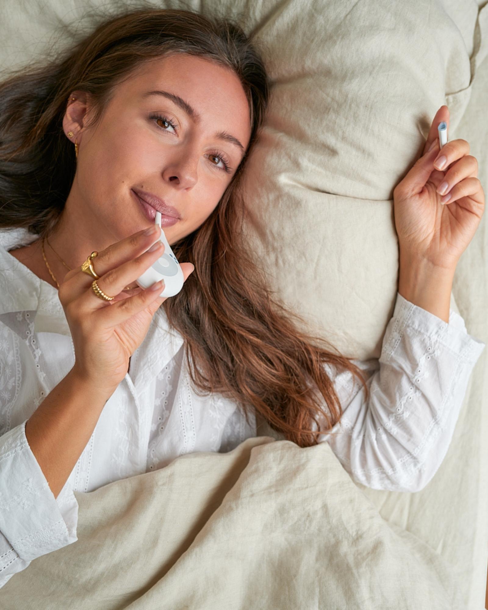 Woman using Daysy fertility tracker in bed for daily morning temperature measurement